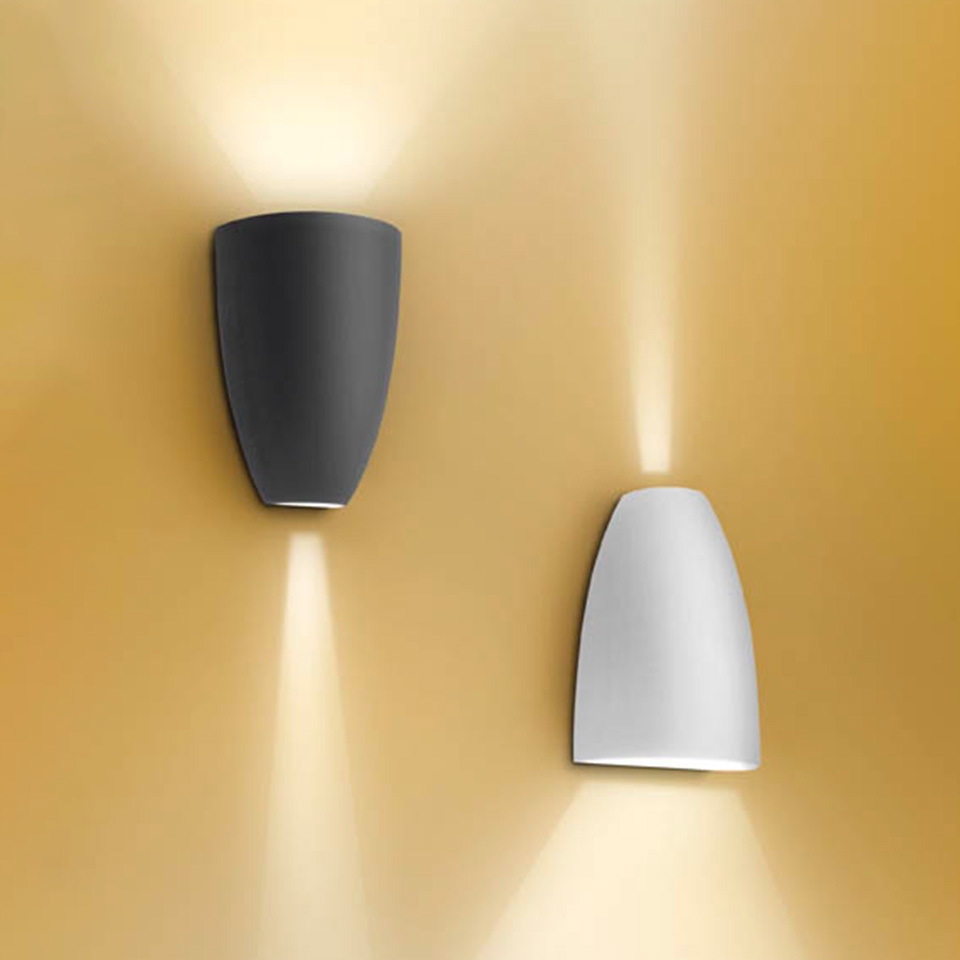 Artemide Molla wall sconces in anthracite and white, emitting warm upward and downward light beams against a golden wall