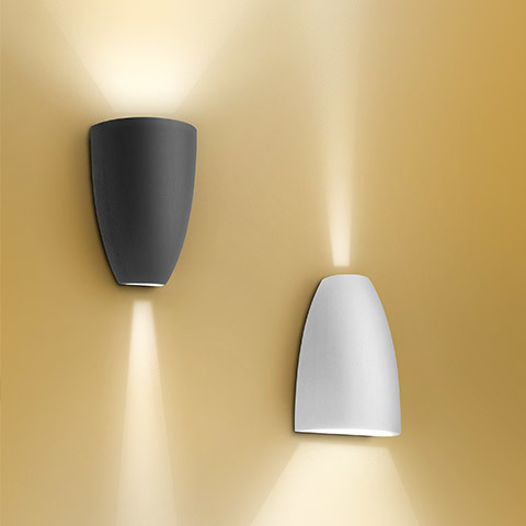 Artemide Molla wall sconces in anthracite and white, emitting warm upward and downward light beams against a golden wall