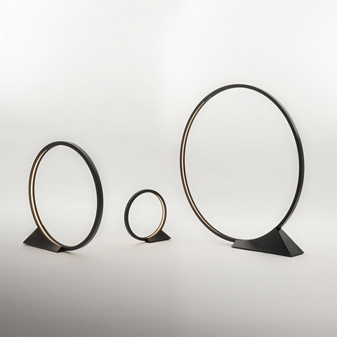 Artemide O table lamps in three sizes: circular black rings with warm LED inner glow, mounted on triangular black bases