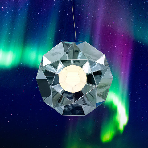 Artemide Arctic pendant lamp with faceted chrome geometric shade resembling a diamond, glowing softly against a northern lights sky