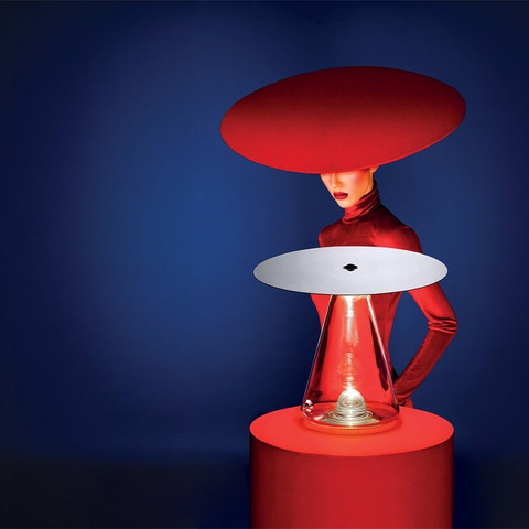 Artemide Boltons table lamp: red conical glass base with white reflective disc shade, styled with a model in red outfit against blue background
