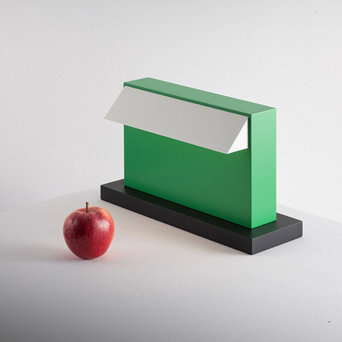 Artemide Hera table lamp in green with white pivoting shade on black base, shown next to a red apple for scale