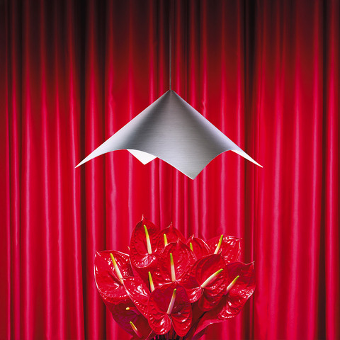 Artemide Iperbole pendant lamp with brushed aluminum angular shade suspended above red anthurium flowers against red curtain