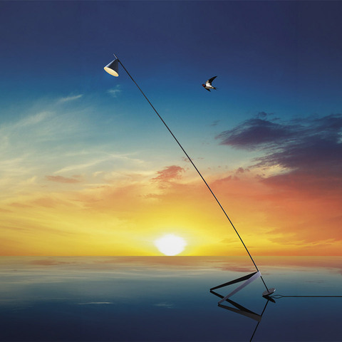 Artemide Vea floor lamp with slim diagonal stem and small conical shade, reflected on water surface against a vibrant sunset sky