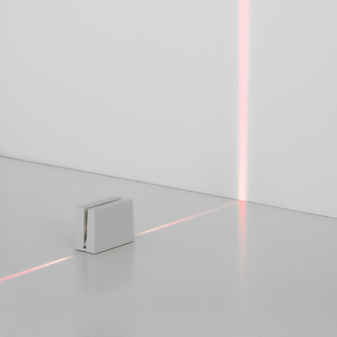 Artemide Antarktikós: compact white floor unit emitting a thin red laser line across the floor and up the wall