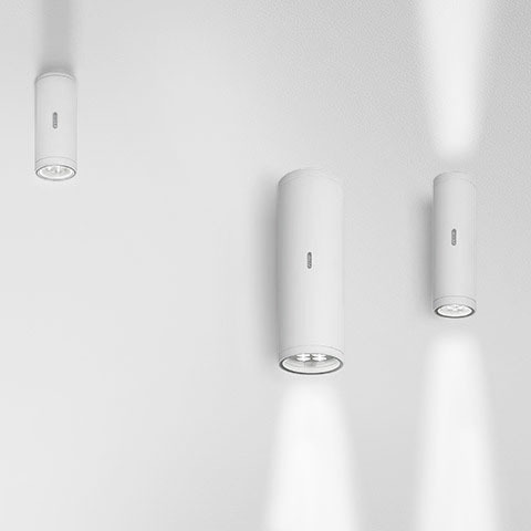 Three Artemide Calumet white cylindrical ceiling spotlights of varying sizes, each projecting a focused beam of light downward.