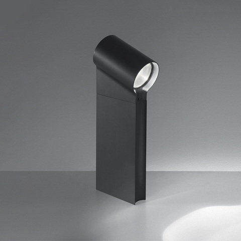 Artemide Oblique dark grey outdoor bollard light with angled cylindrical LED head casting a focused beam on the ground