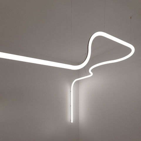Artemide Alphabet of Light: glowing white LED tube bent into an abstract suspended shape, with a vertical drop element, against white walls