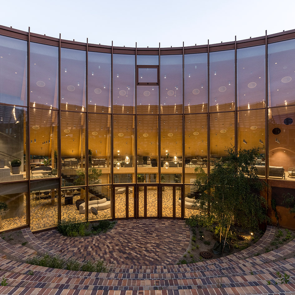 Curved glass facade of an elegant interior space at dusk, featuring warm ambient lighting with pendant lamps and seating areas inside.
