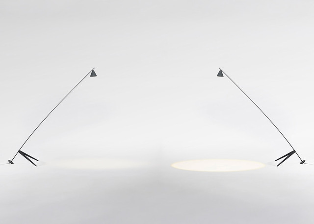 Two dark minimalist floor lamps with long angled arms and conical shades, casting focused light pools on a white surface.