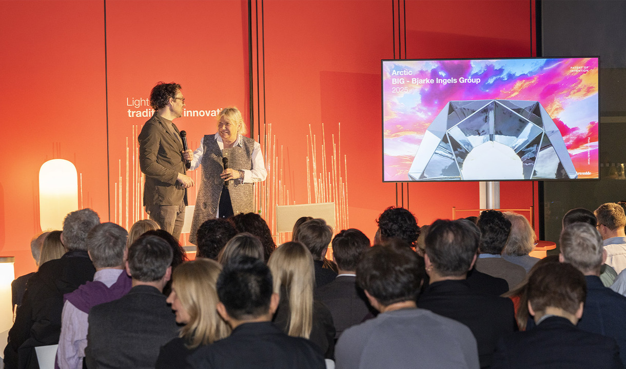 Carlotta de Bevilacqua and Jakob Lange speak on stage in front of an audience seen from behind, during a presentation with a screen in the background.