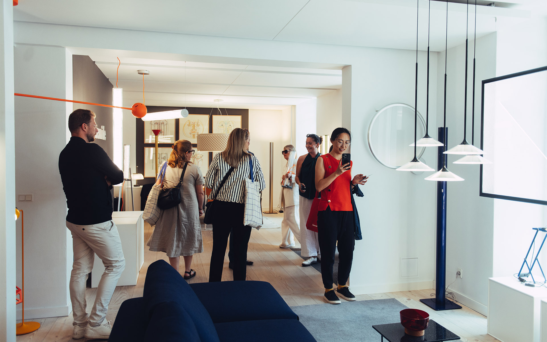 Visitors exploring an Artemide showroom featuring pendant and floor lamps in white, orange, and blue tones on display.
