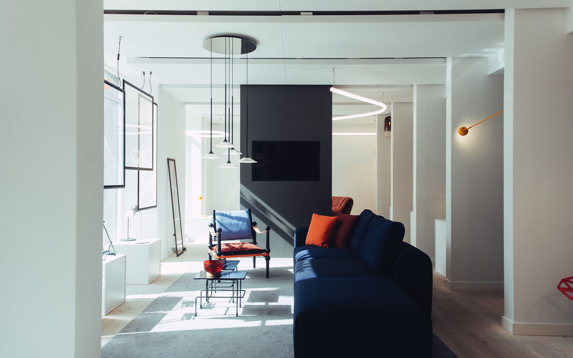 Modern living room with Artemide circular LED pendant, thin black pendants, and a gold wall lamp above a navy sofa with red cushions