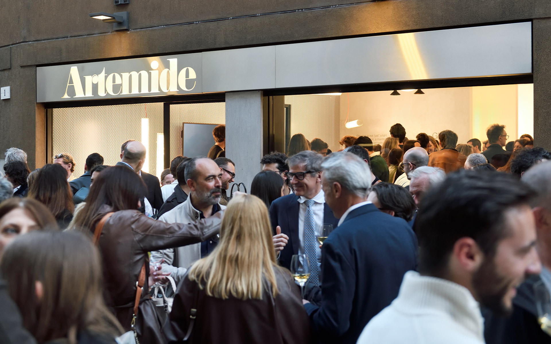 Crowd of guests gathered outside an Artemide store during a public event or opening, with the illuminated brand sign above.