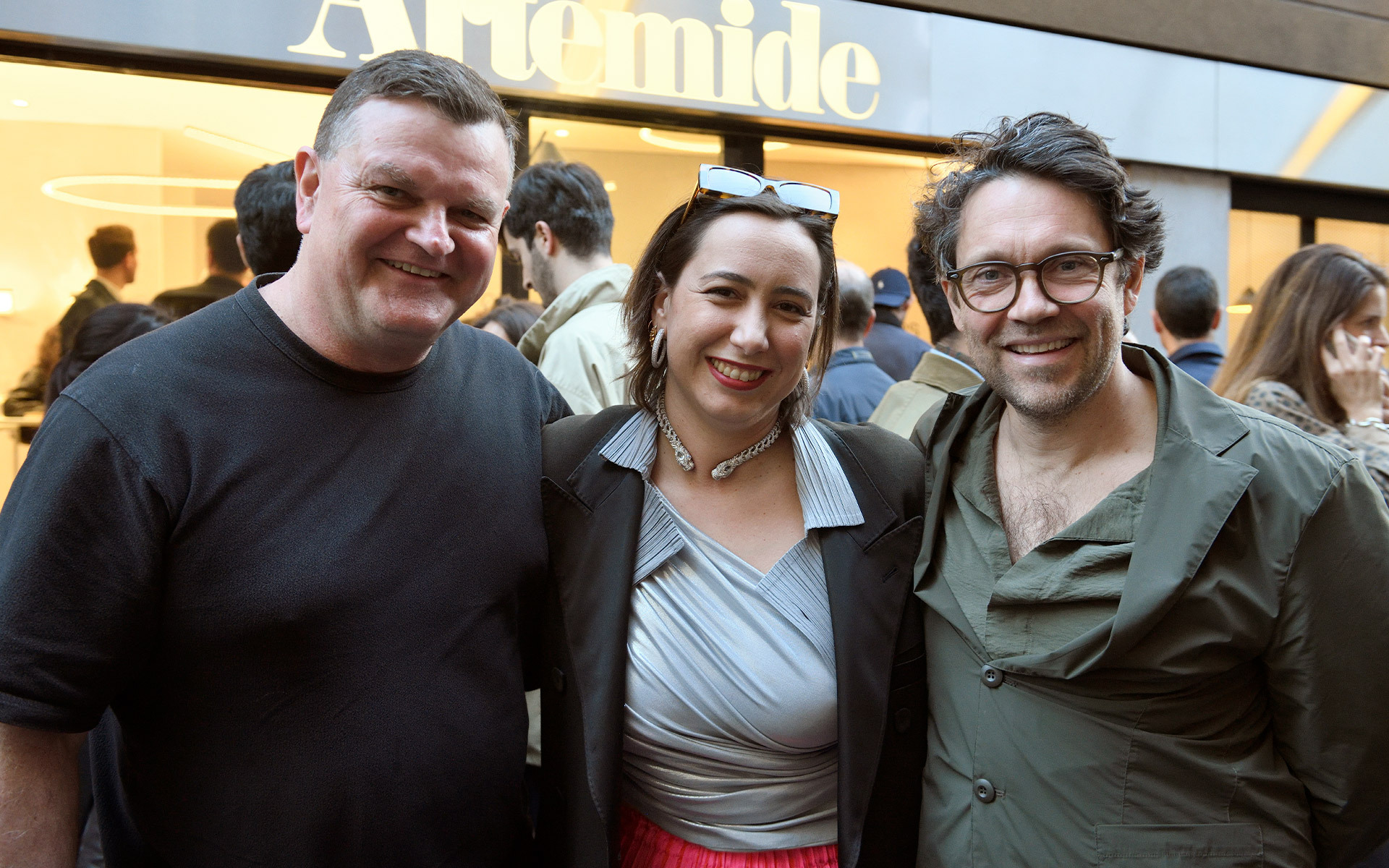 Three people smiling together in front of an Artemide store entrance at an event.