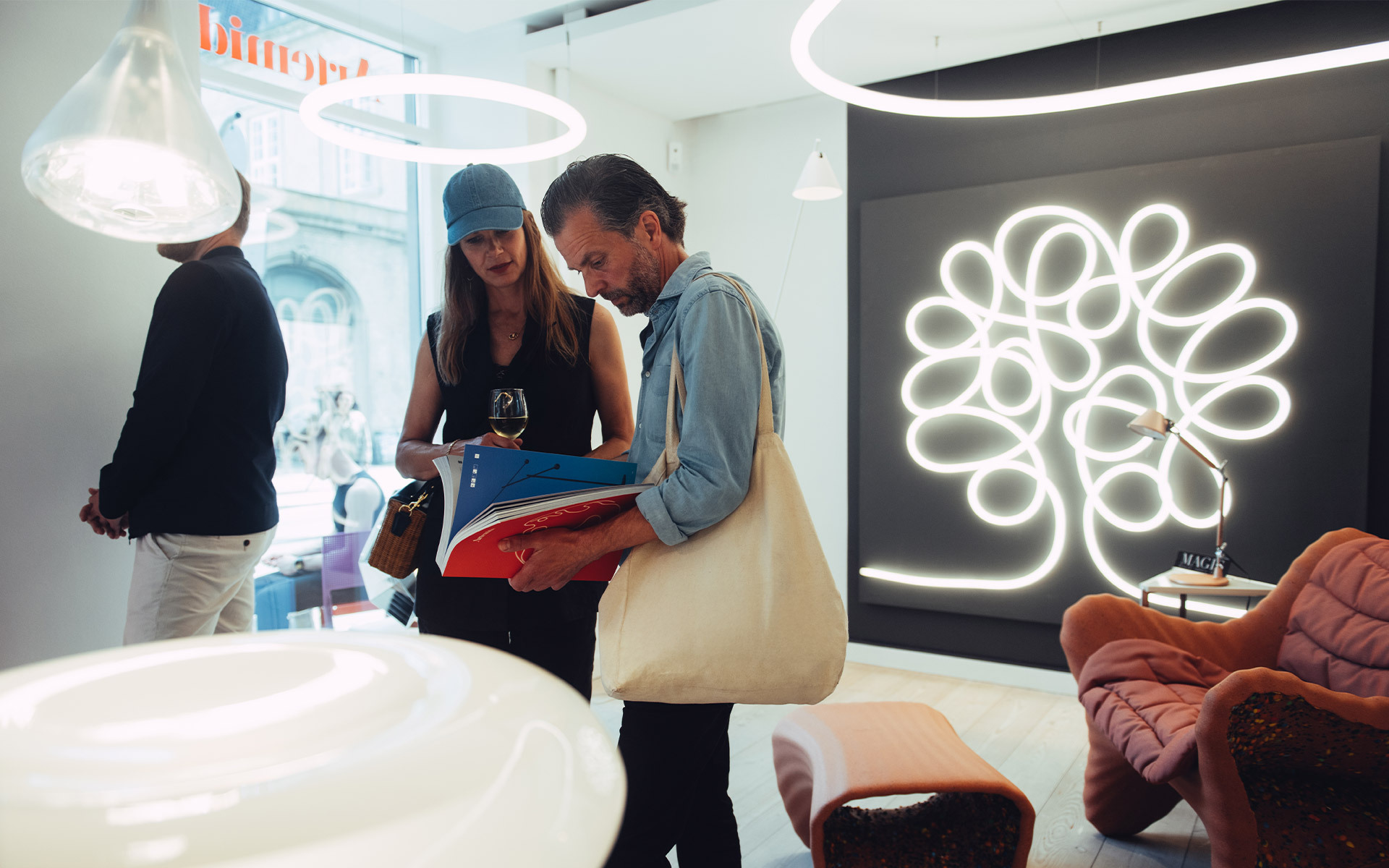 Visitors browse catalogs in a showroom featuring an Artemide tree-shaped LED wall light and circular pendant lamps.