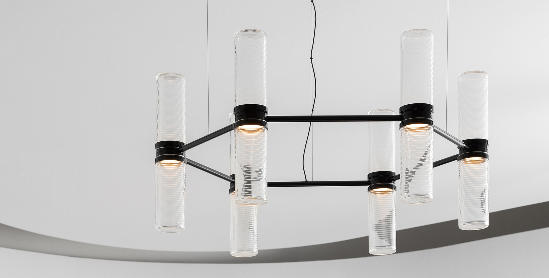 Pendant chandelier with black rectangular frame holding eight vertical clear glass cylindrical tubes with warm LED light sources