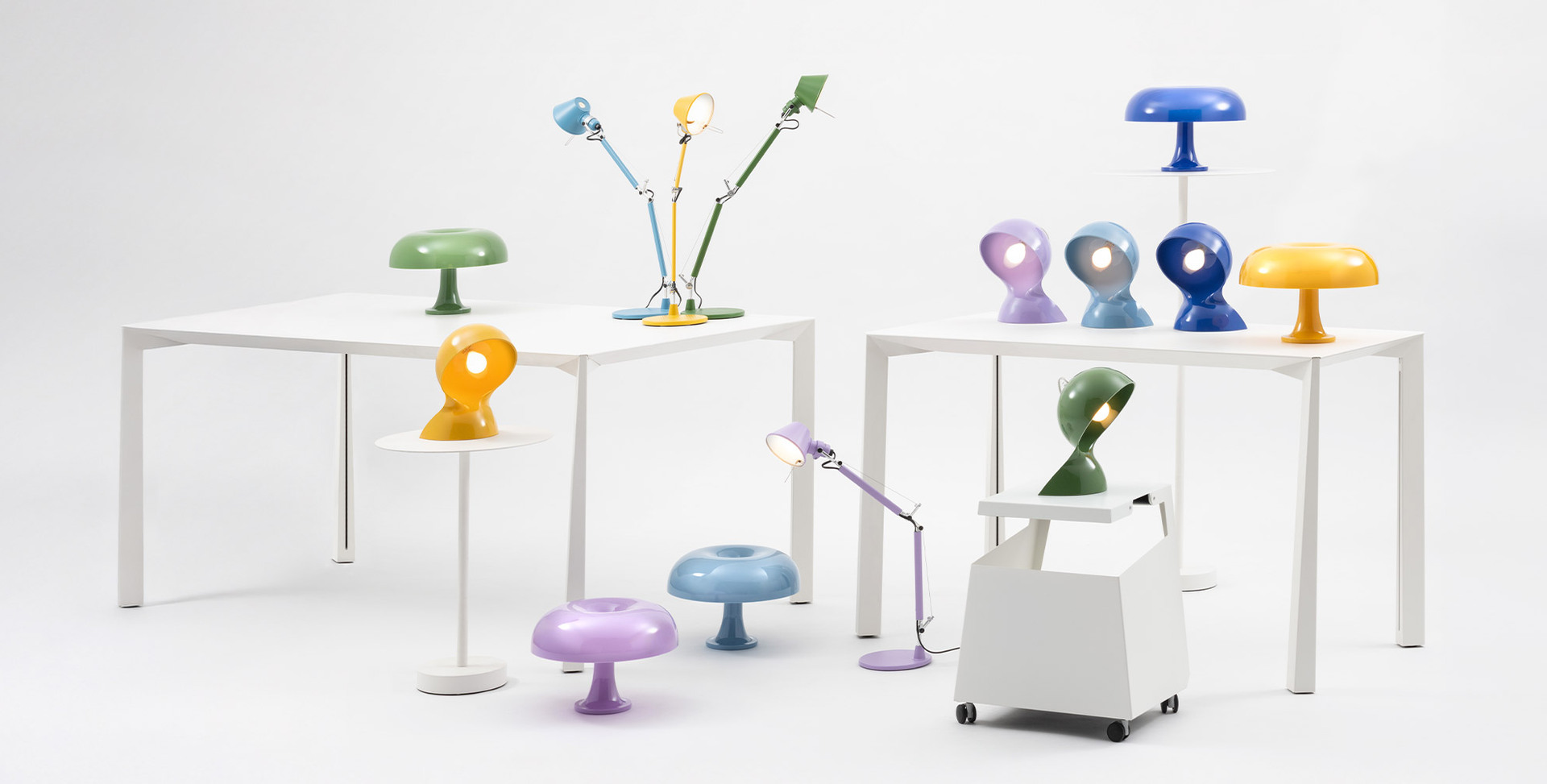 Composition of Dalù, Nessino and Tolomeo lamps in various colors, arranged on white tables against a neutral background