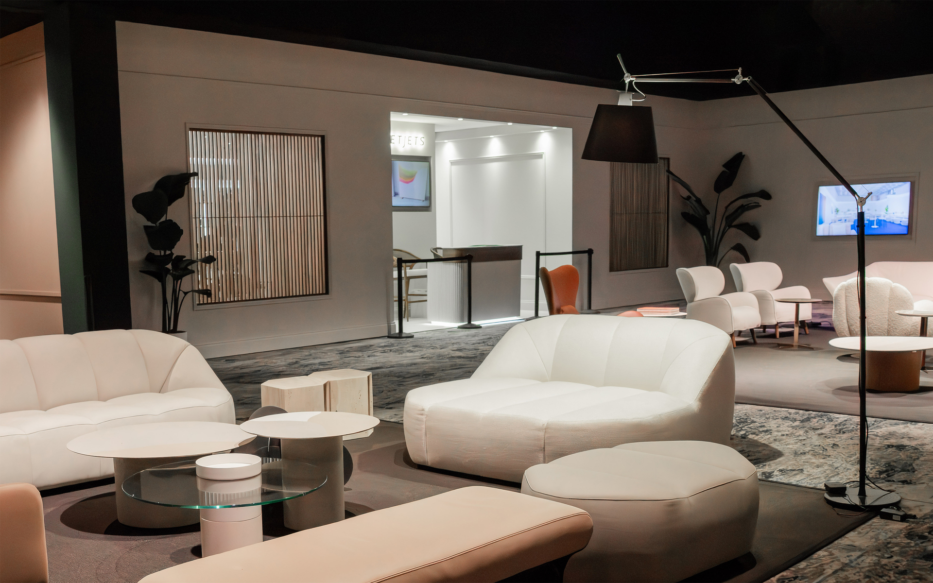Modern lounge with white curved sofas, glass coffee tables, and a large black floor lamp with adjustable arm in the foreground