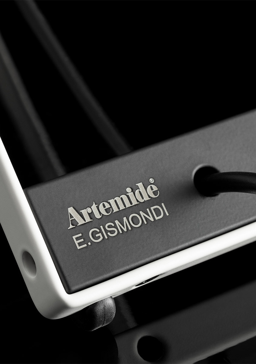 Close-up of the base of the Sintesi lamp featuring the inscription "Artemide, E. Gismondi", against a black background.