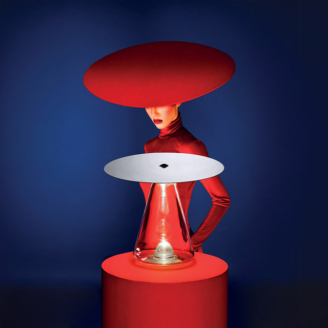Artemide table lamp with transparent conical base and flat disc shade on red pedestal, styled with a model in red wearing a matching wide-brim hat