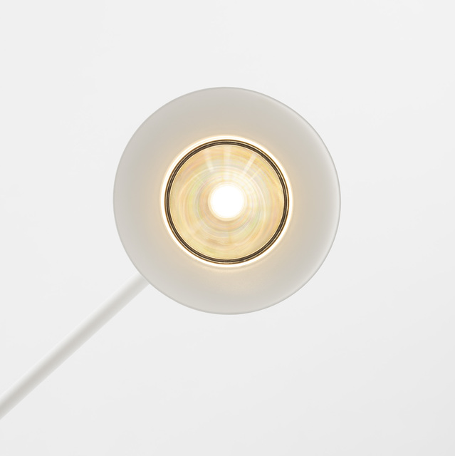 Close-up of a white circular lamp head viewed from above, featuring a central LED bulb with iridescent reflector and warm glow