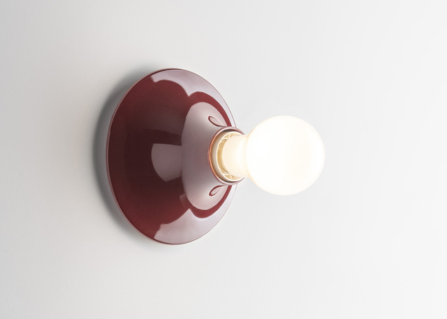 Bordeaux Teti wall lamp with a lit spherical bulb, mounted on a white wall.