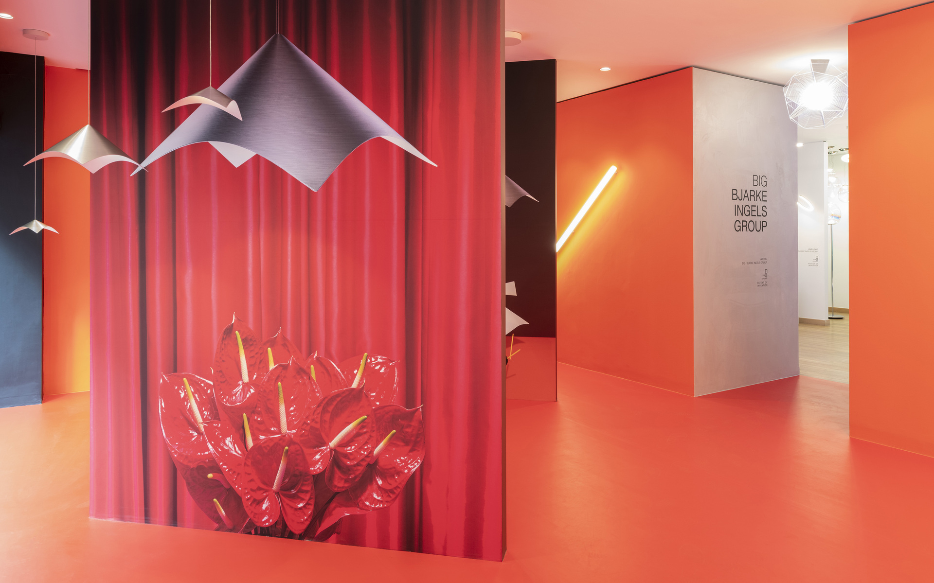 BIG Bjarke Ingels Group office with Artemide pendant lights, origami-shaped fixtures, and a linear wall lamp in a vibrant orange corridor