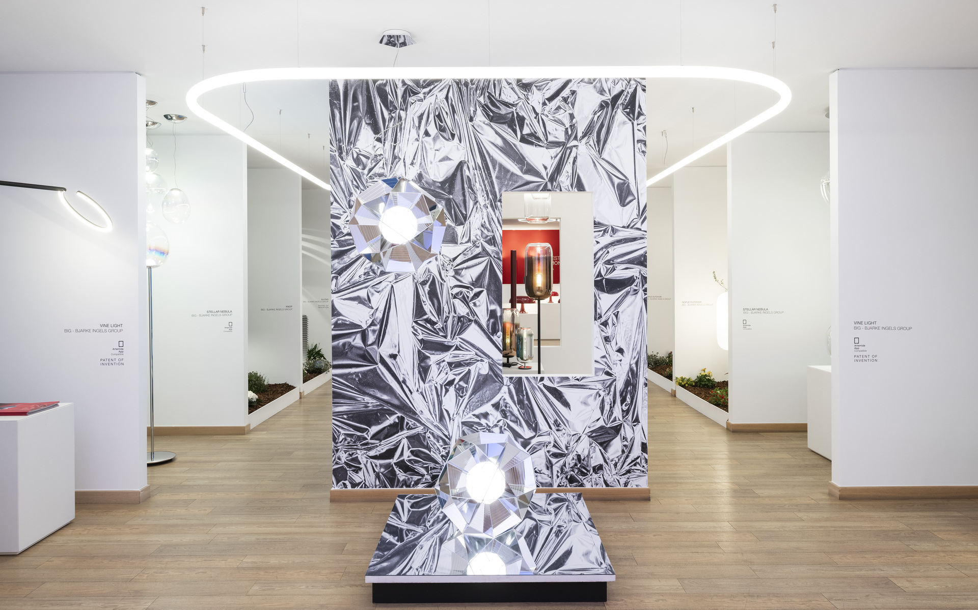 Artemide showroom display with oval LED ring pendant, two faceted crystal-like table lamps on metallic crinkled backdrop