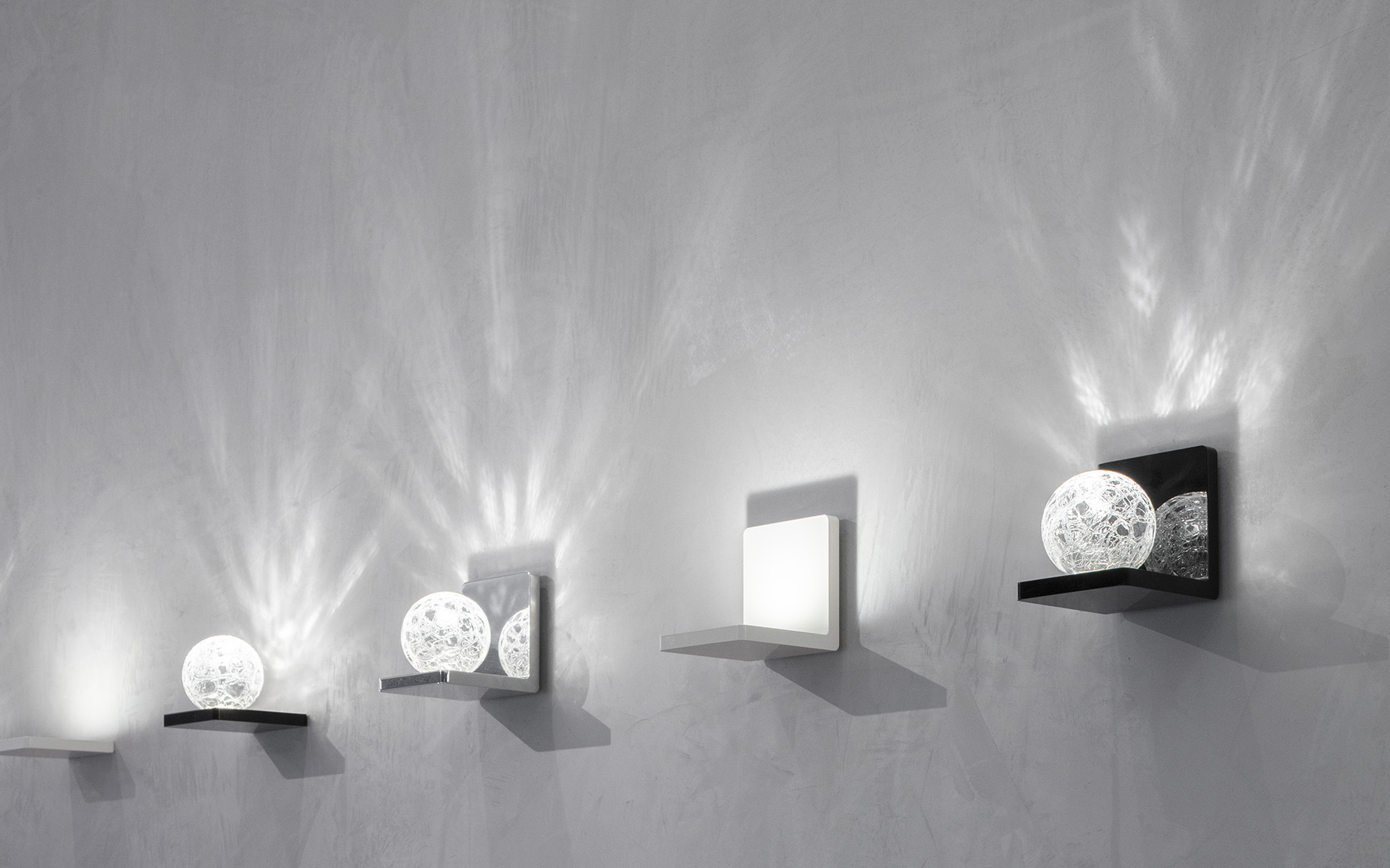 Four Artemide wall sconces mounted on a grey wall, featuring spherical mesh and square diffusers casting dramatic radial light patterns.