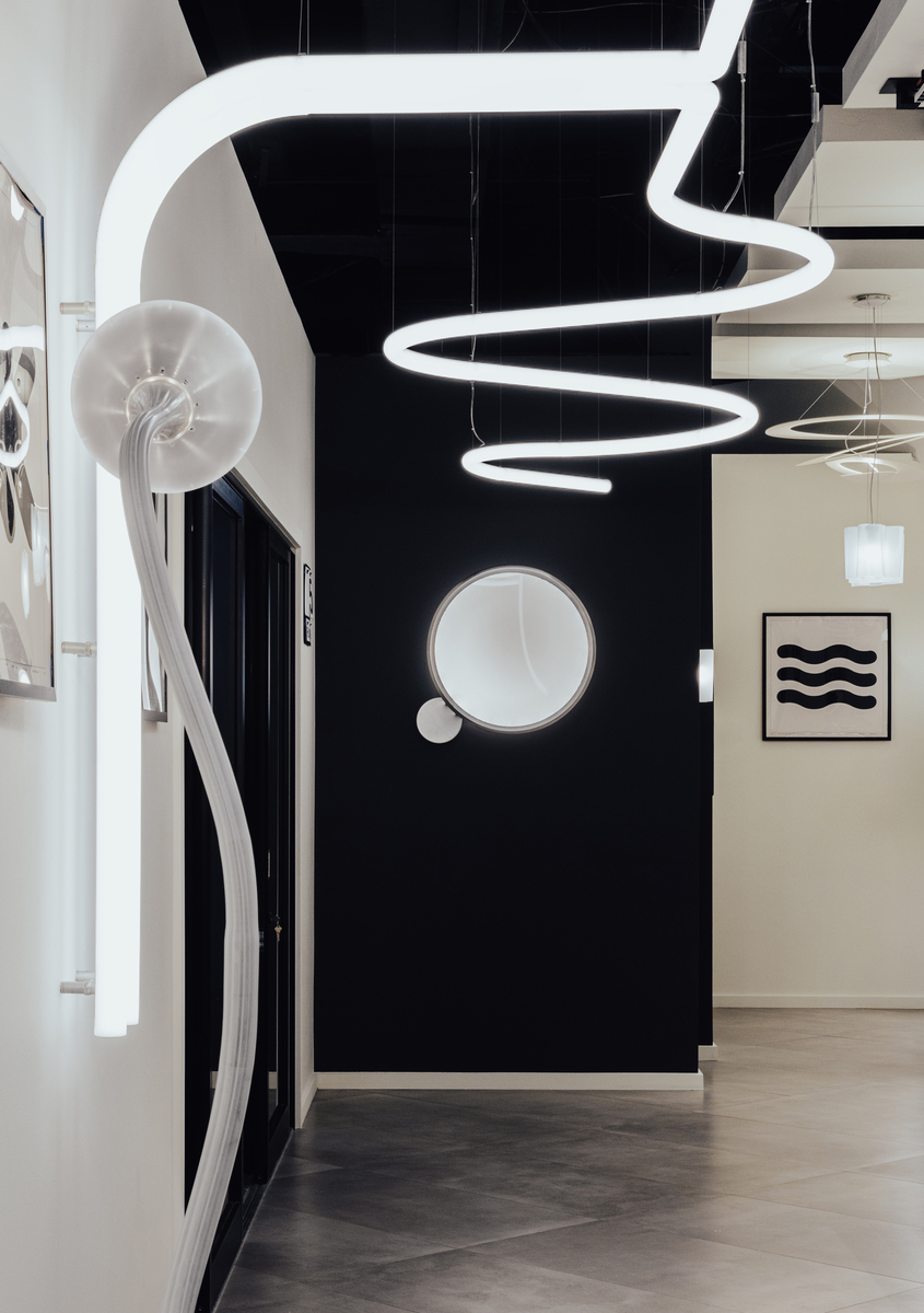 Artemide showroom with spiral pendant light on black ceiling, circular wall lamp, and shell-shaped sconce on white arch