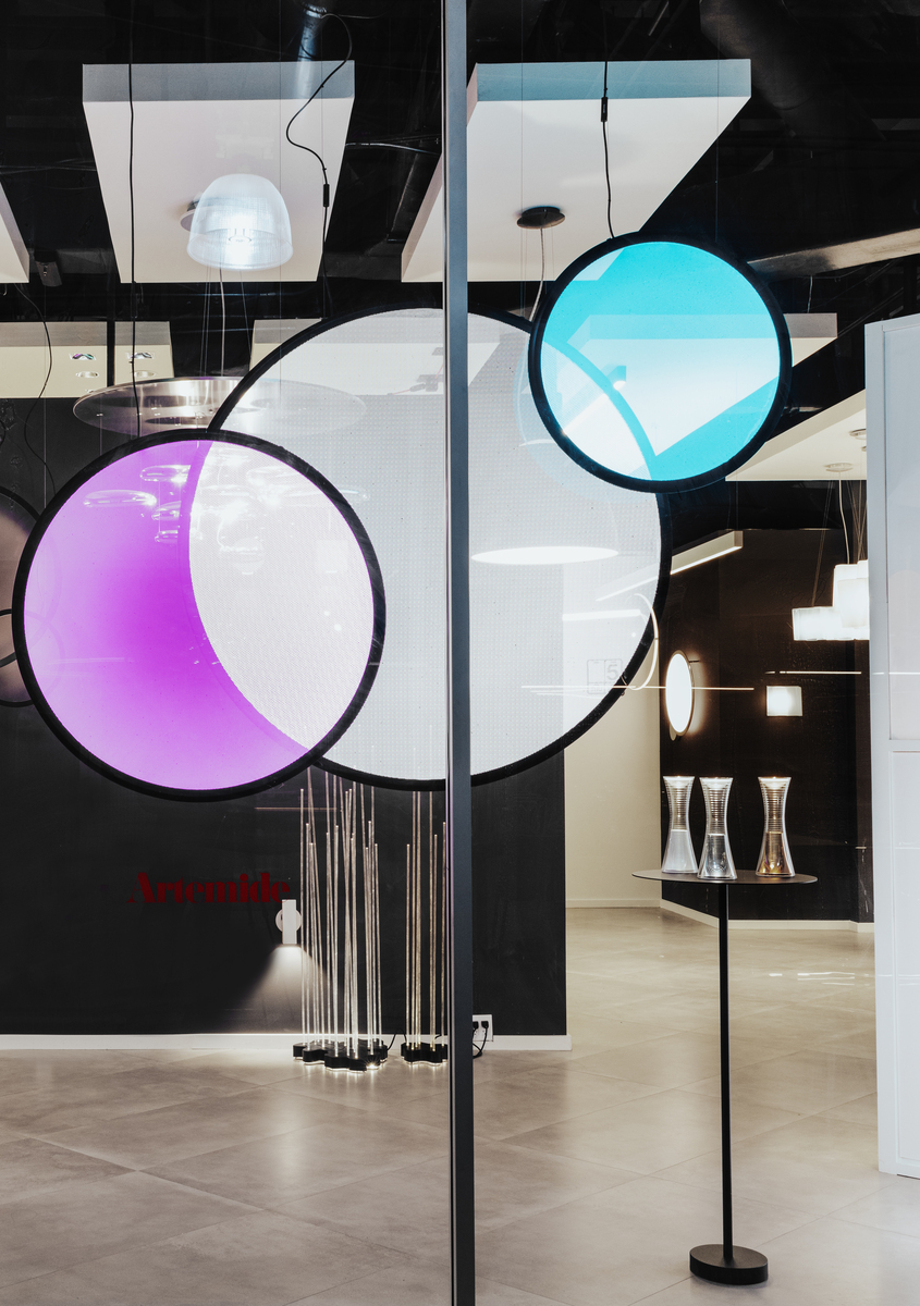 Artemide showroom displaying large circular pendant lamps glowing in purple and cyan, with floor lamps and smaller fixtures in background