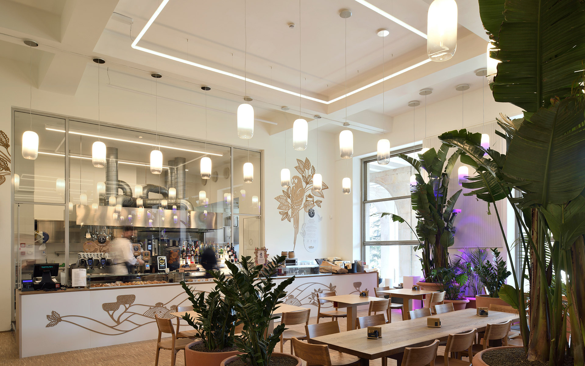 Modern café interior with Artemide pendant and wall lights, geometric LED ceiling lines, lush plants, and dining tables.
