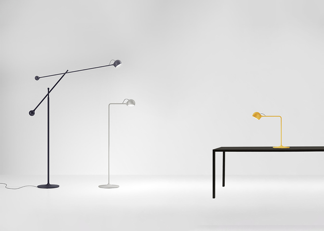 Three Artemide lamps: dark articulated floor lamp, white reading floor lamp, and yellow desk lamp on a black table