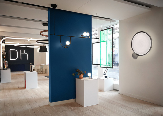 Artemide showroom with pendant lamp with globe bulbs, large round wall light, and table lamps displayed on white plinths.