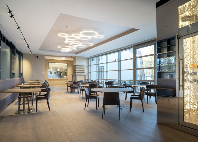 Modern restaurant interior with circular LED pendant lights on ceiling, track lighting on left wall, large windows, and dark wood furniture.