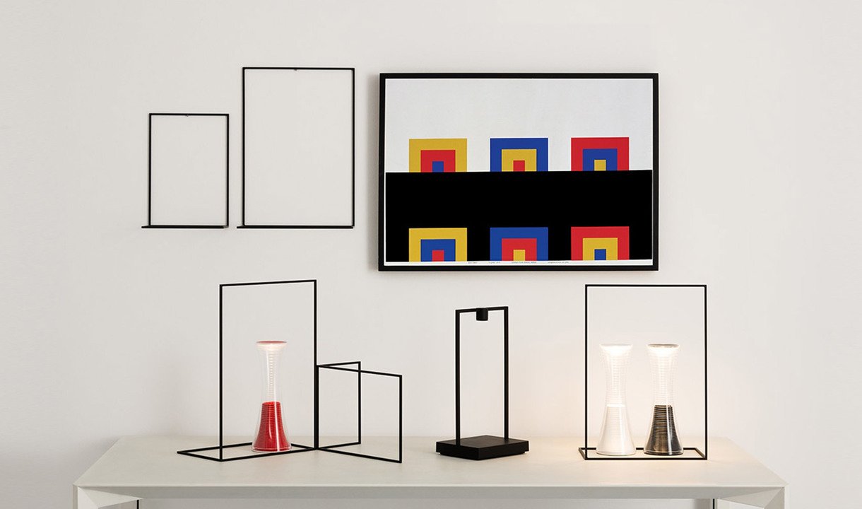 Three Artemide table lamps with minimalist black wire frames on a white surface, featuring red, black, and white conical shades