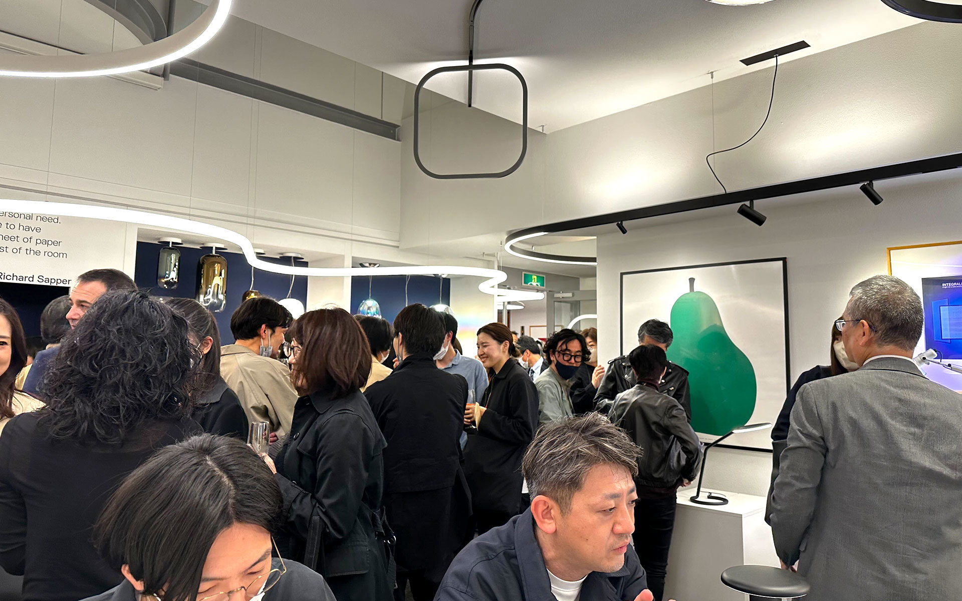 Crowded Artemide showroom event with guests mingling under circular and square pendant lights on the ceiling.