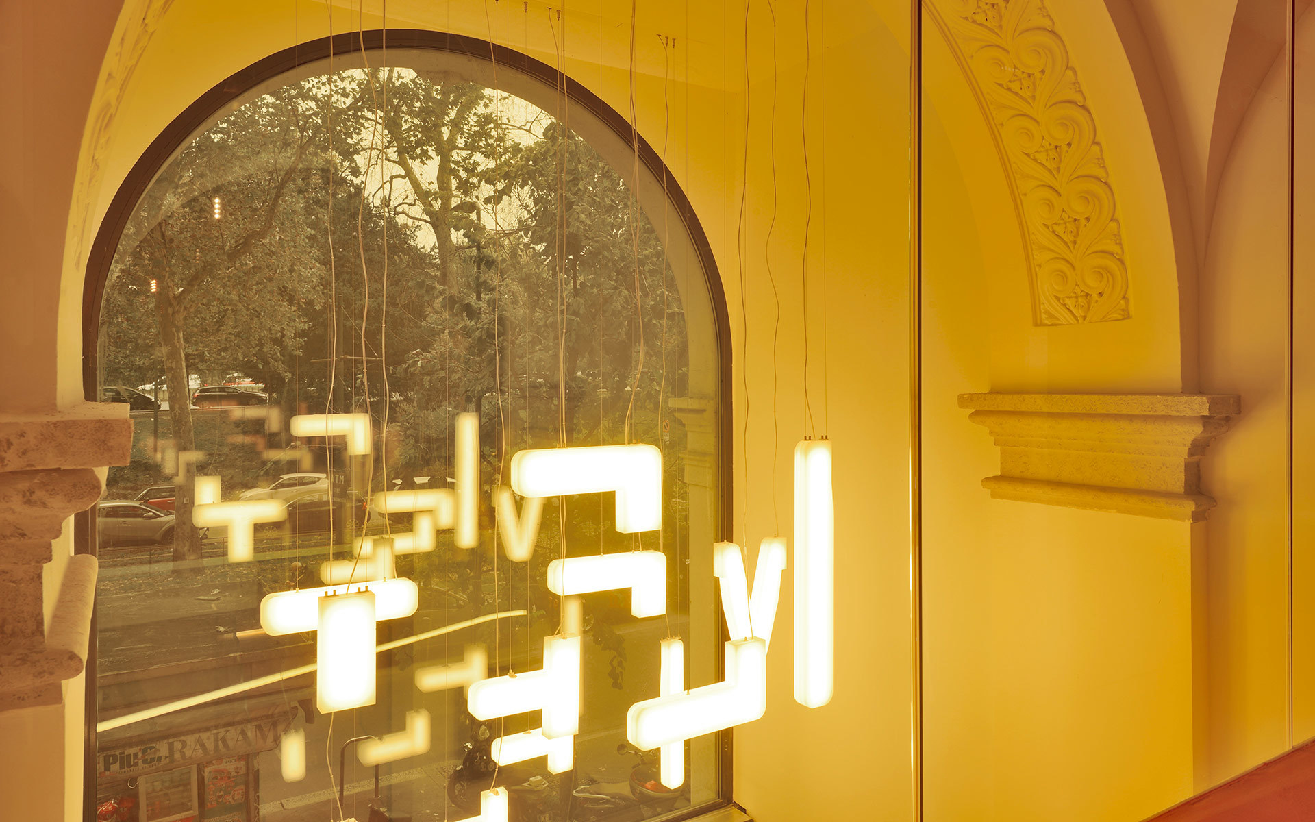 Artemide pendant lights with glowing geometric LED modules suspended before an arched window, casting warm golden light.