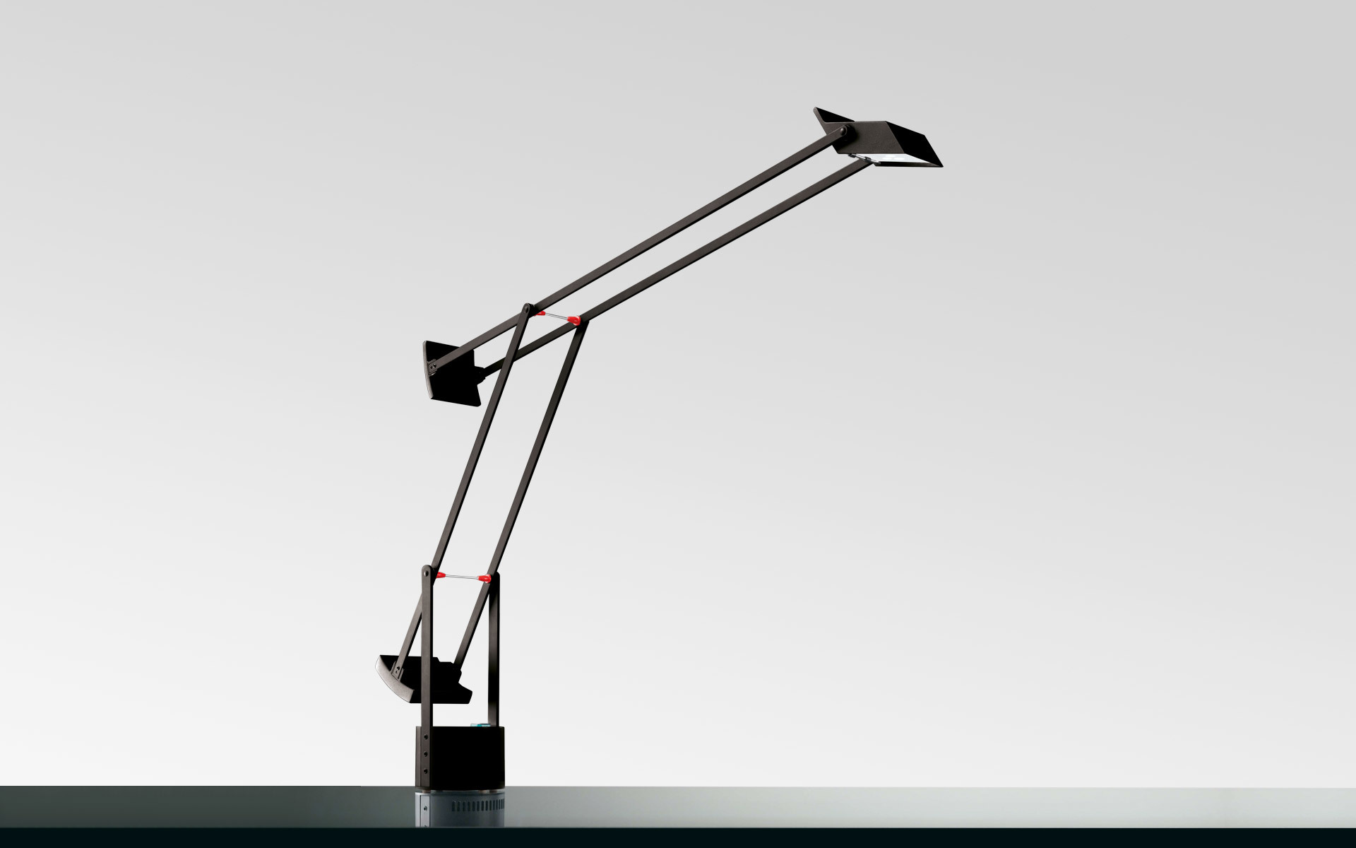 Artemide Tizio black desk lamp with double articulated arm, red joints, and flat head, balanced on a weighted base