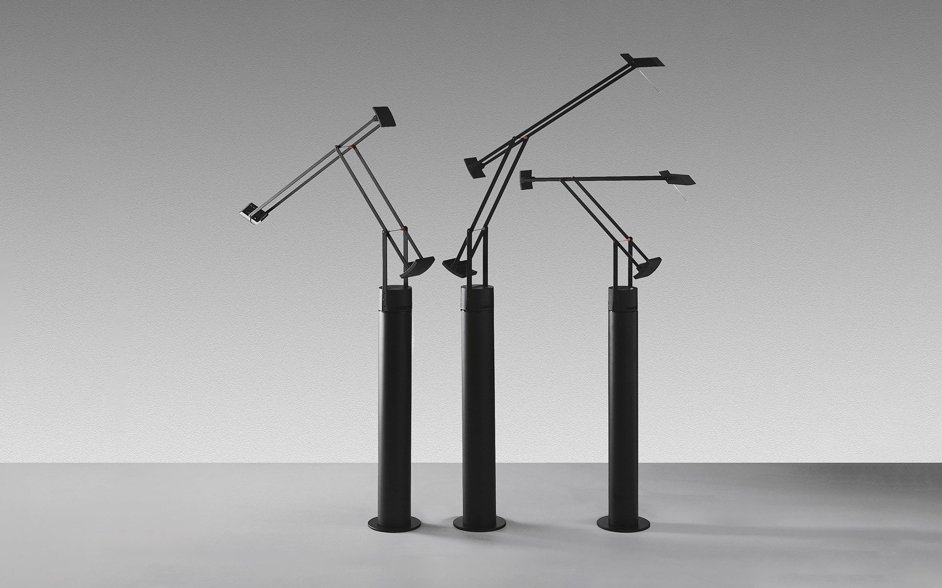 Three Artemide Tizio floor lamps in black, featuring iconic counterbalanced adjustable arms on cylindrical bases, shown in different positions