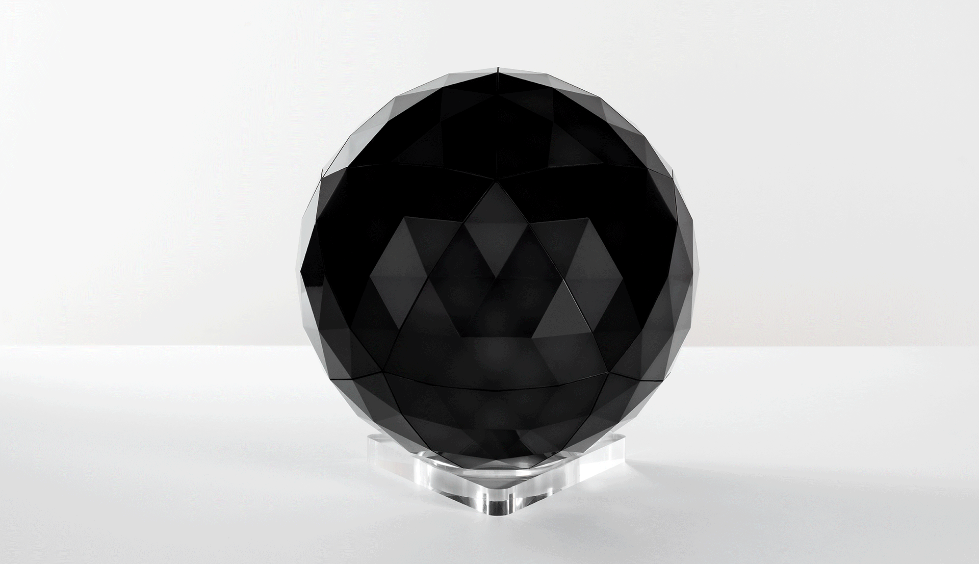 Artemide spherical table lamp with geodesic triangular metal frame diffusing soft white light, mounted on a transparent crystal base