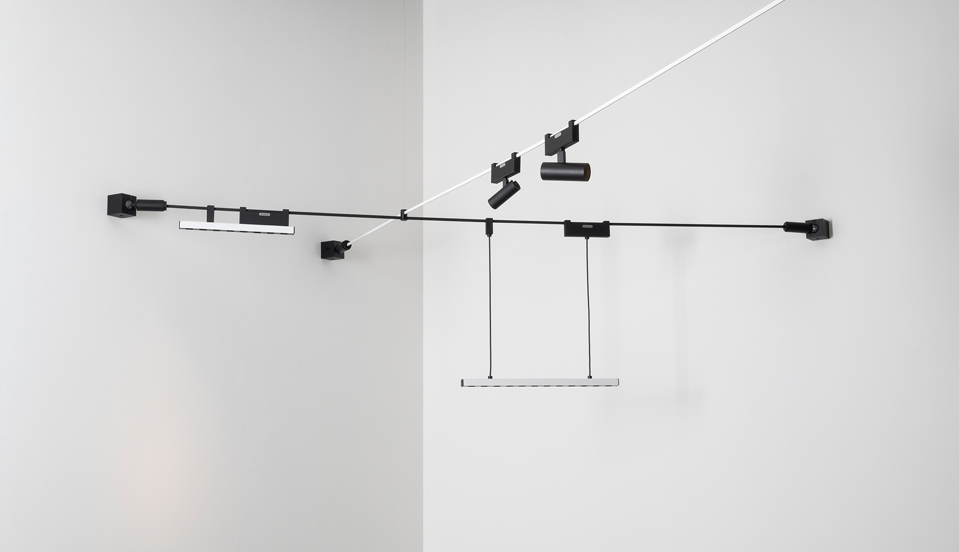 Artemide black track lighting system mounted on white walls, featuring spotlights, a linear LED bar pendant, and cable suspension elements