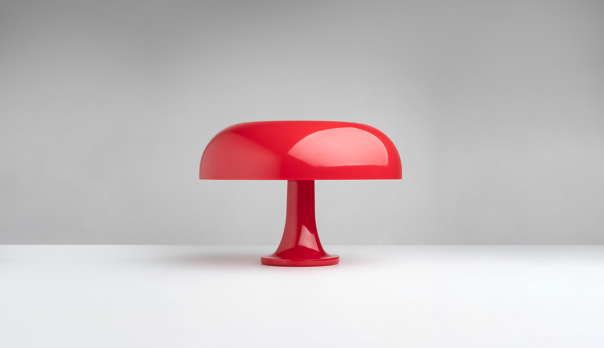 Artemide Nessino table lamp in glossy red, featuring iconic mushroom-shaped shade on a trumpet base