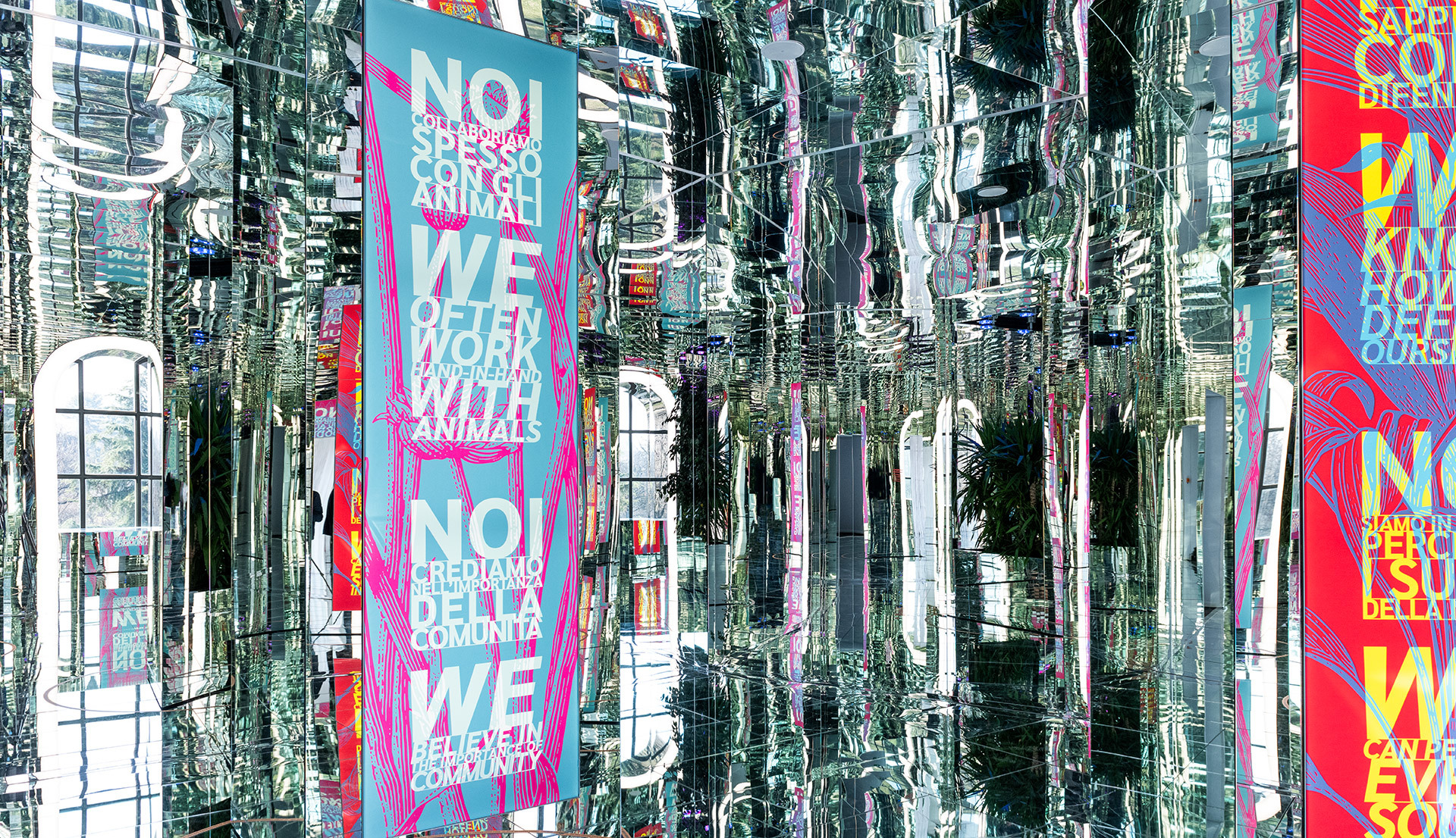 Immersive mirrored installation with hanging colorful banners displaying bilingual text about community and animals