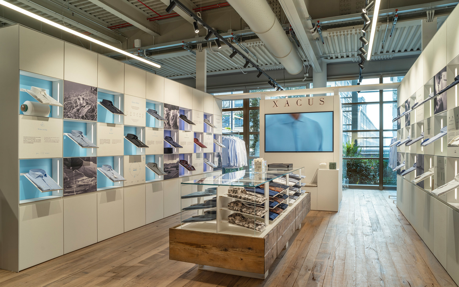 Xacus shirt store interior with Artemide linear LED ceiling lights illuminating display walls and central wooden merchandise table.