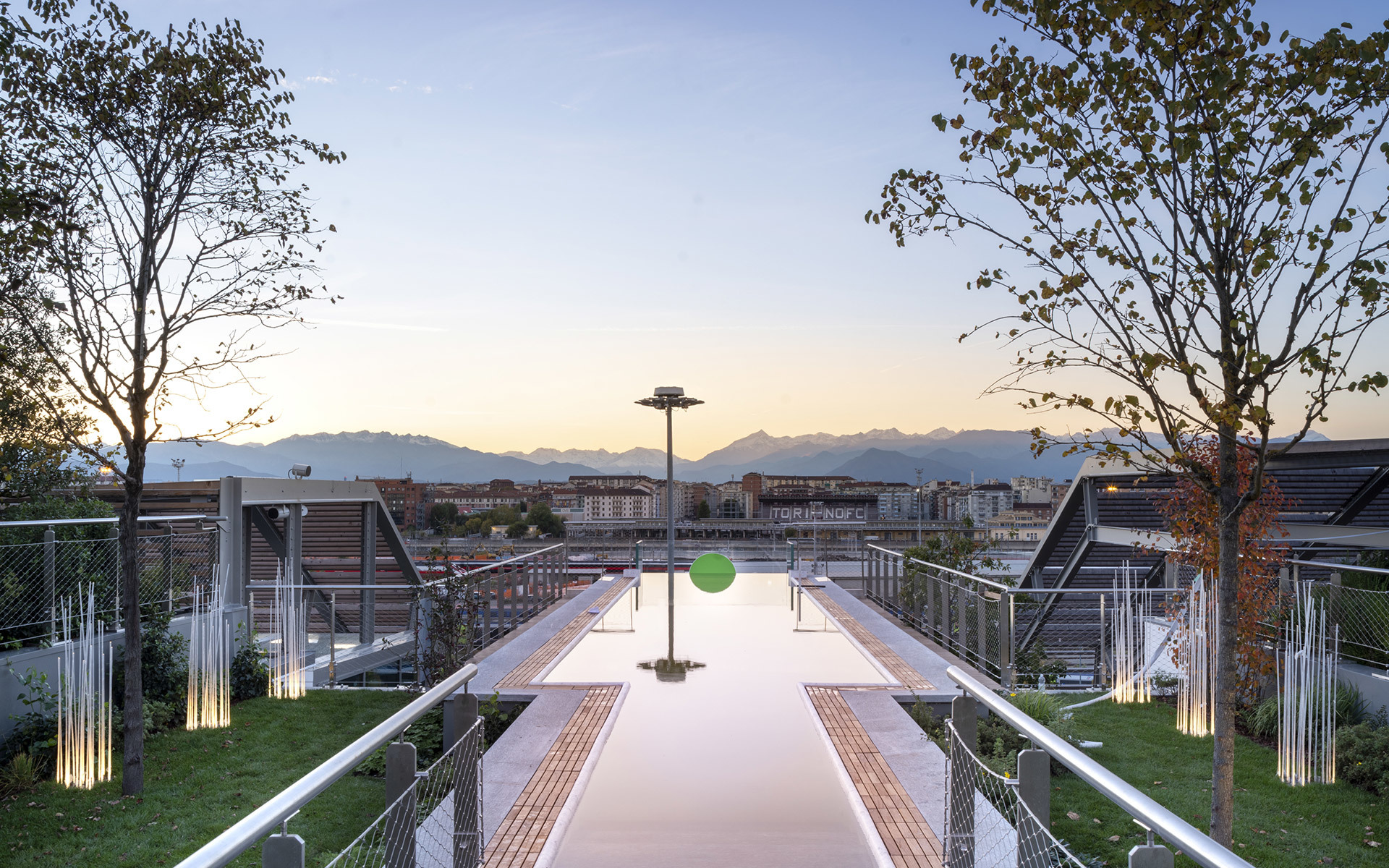 Rooftop terrace at dusk with reflective pool, Artemide outdoor lights, lush greenery, and mountain panorama in background