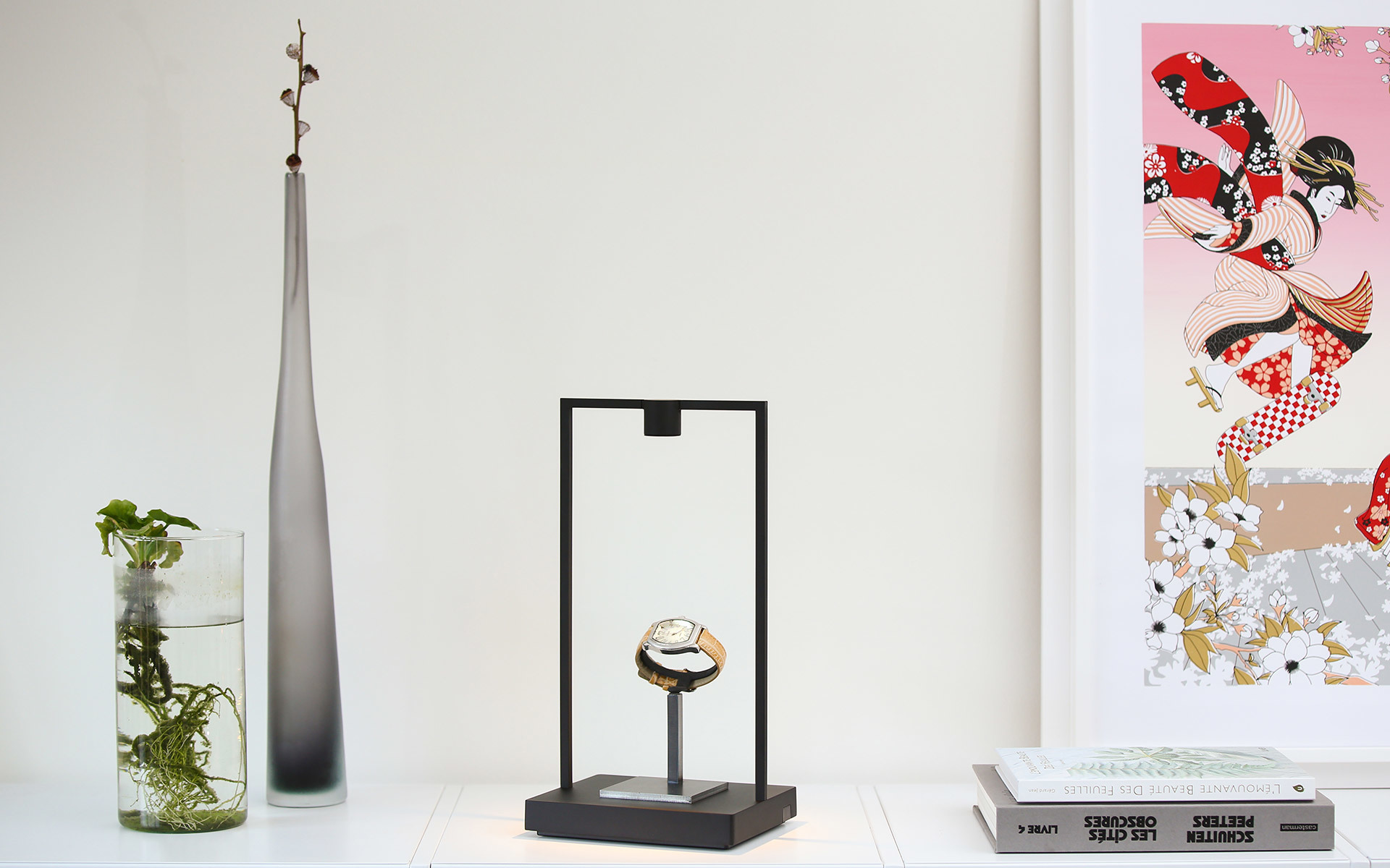 Black rectangular frame table lamp displaying a watch, styled as a minimalist display stand on a white shelf with decorative objects
