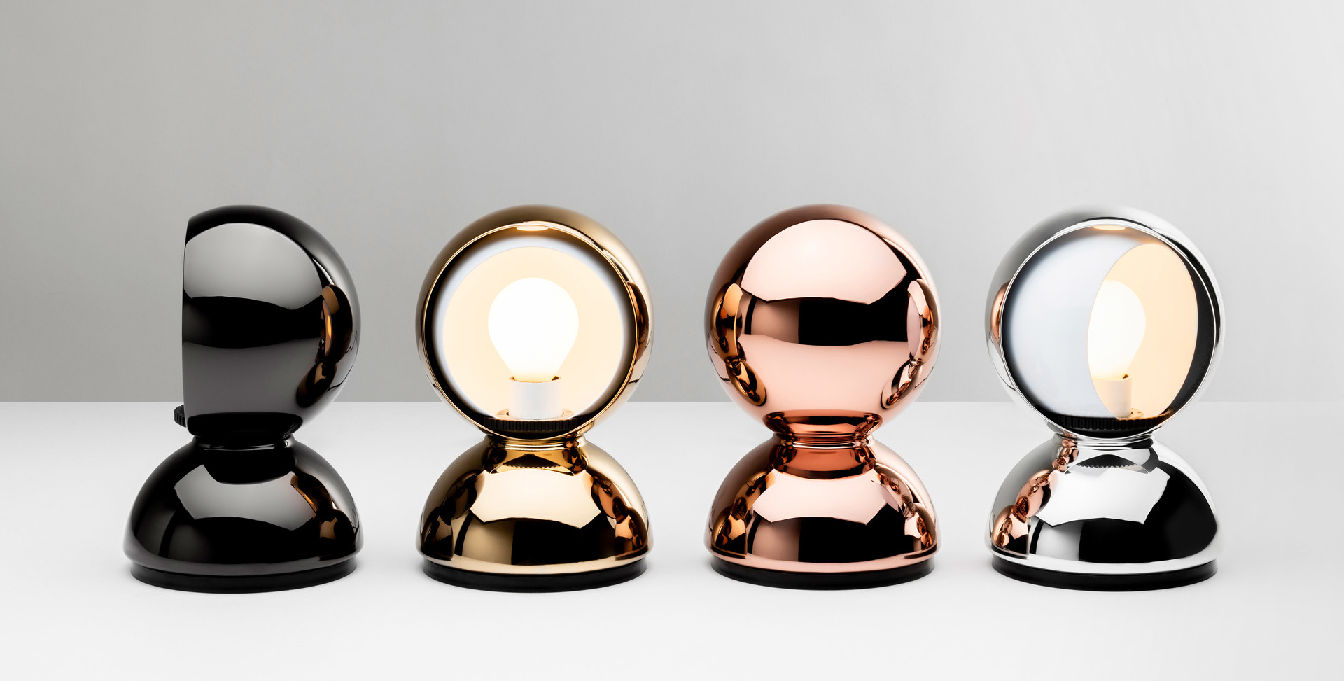 Four Artemide Eclisse table lamps in a row: black, gold, copper, and silver finishes, with rotating spherical shade revealing bulb