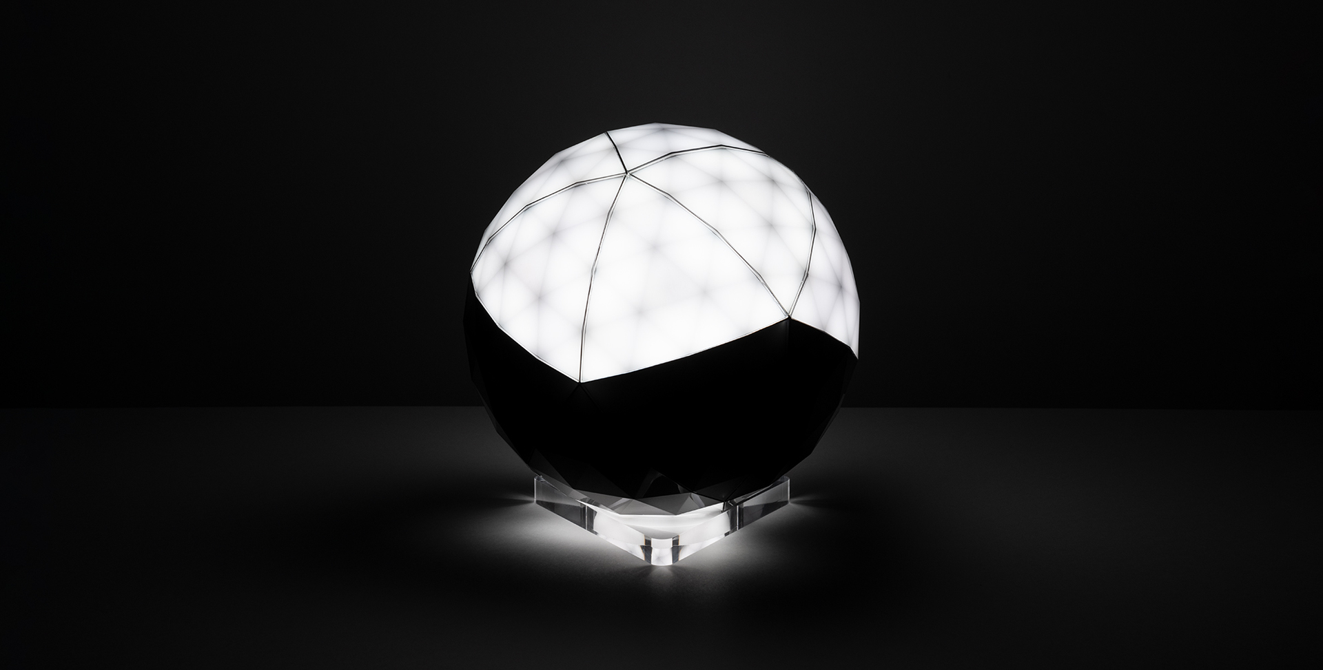 Artemide spherical table lamp with segmented white luminous upper half, dark lower half, on a transparent acrylic base